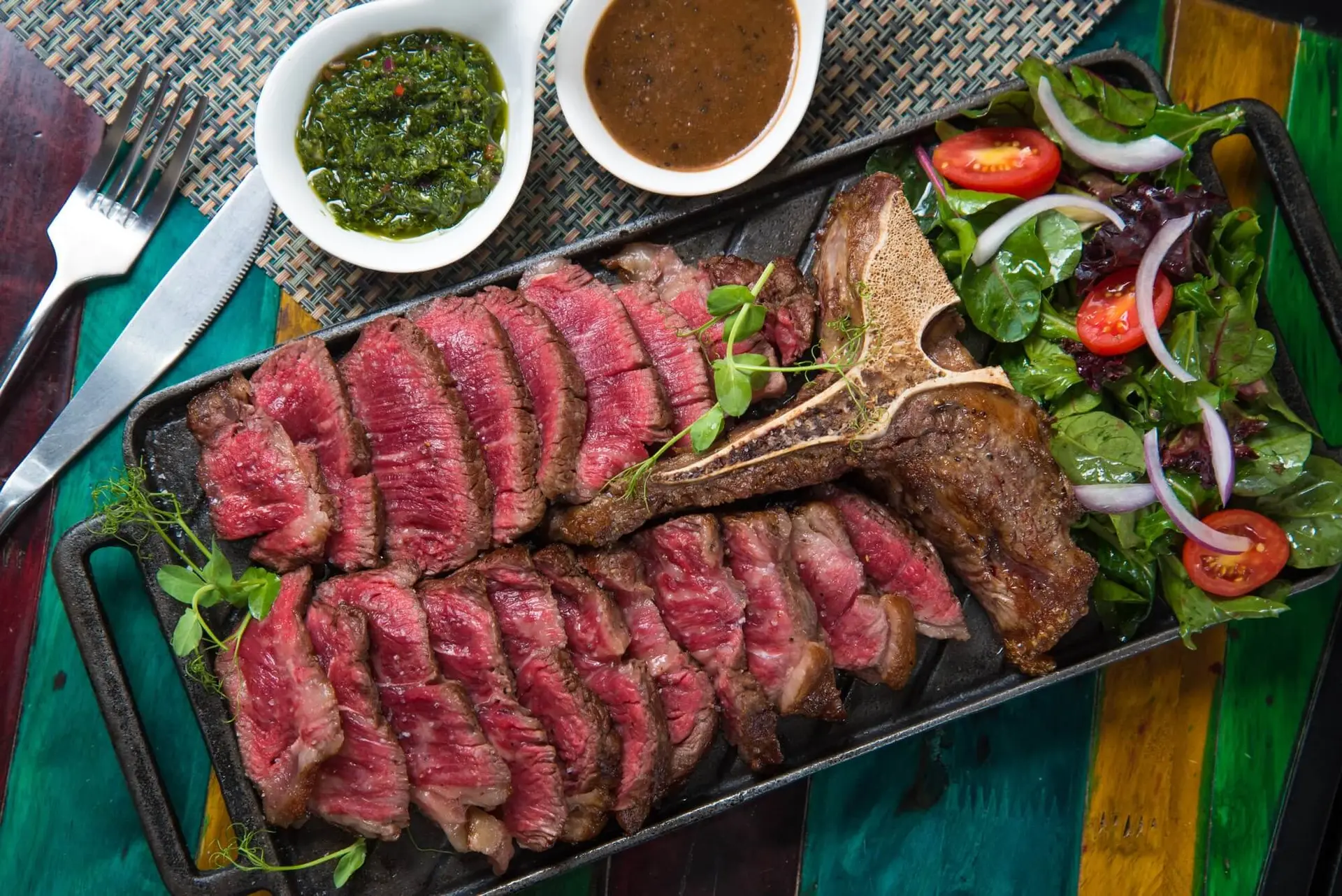 Sliced wagyu steak on cast iron with chimichurri and salad at The Den