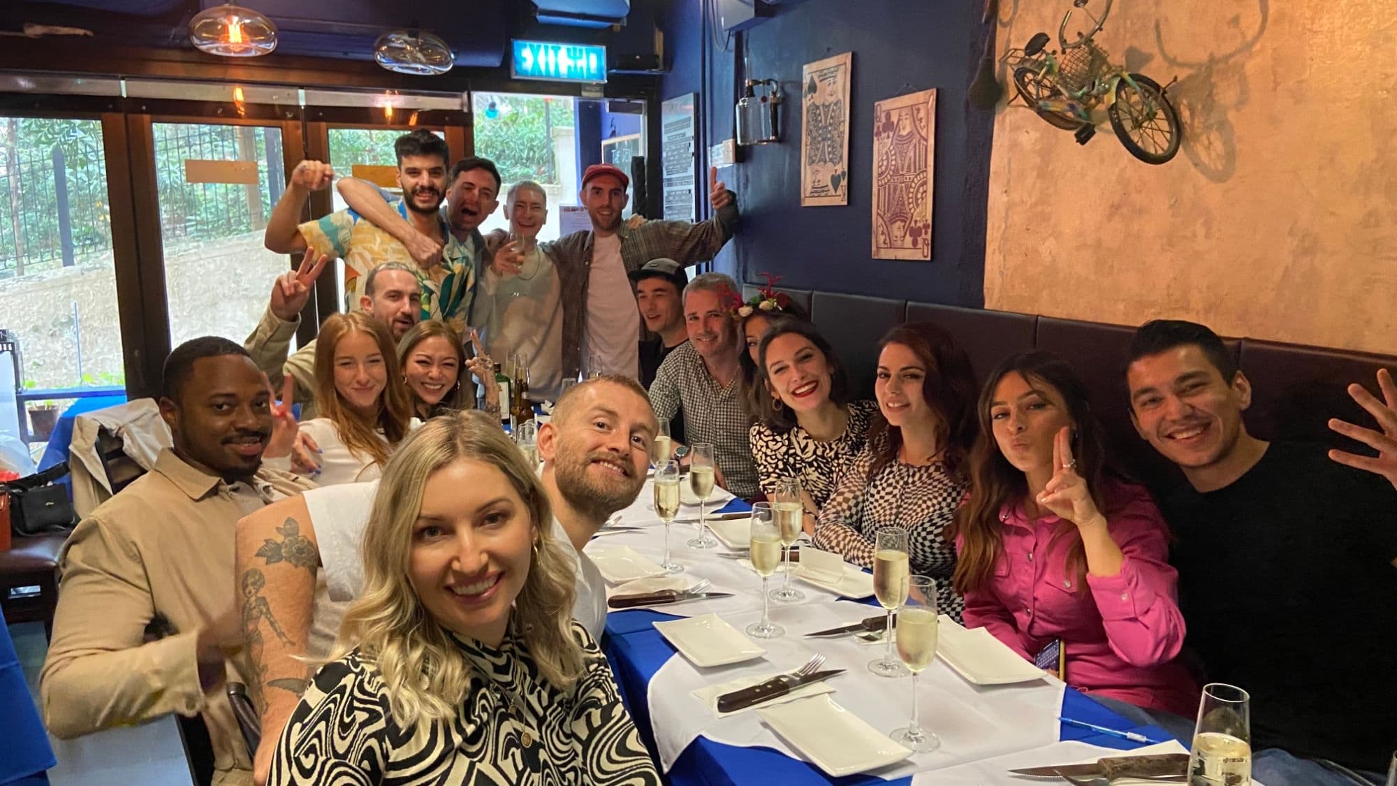 A big group of friends celebrating with champagne around a long table at The Den
