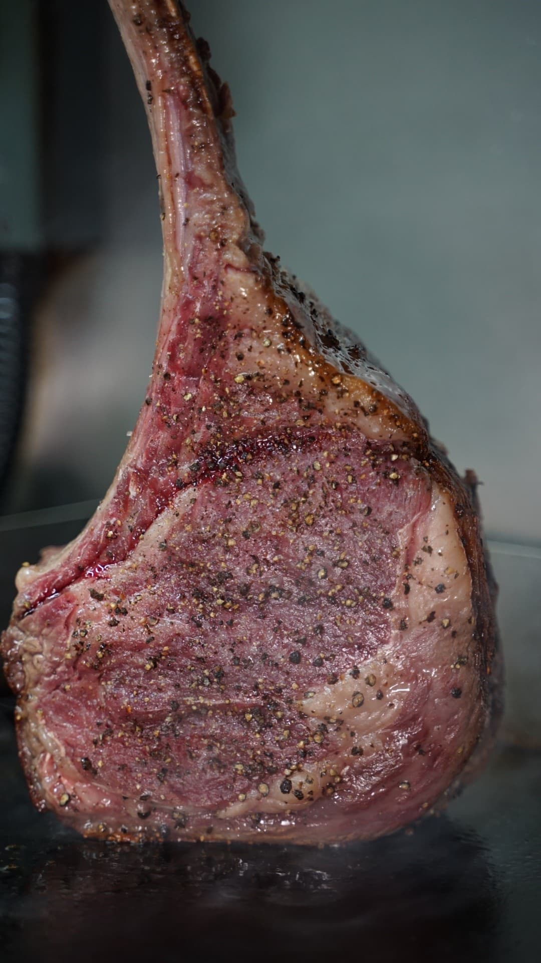 A pepper-crusted tomahawk steak searing at The Den